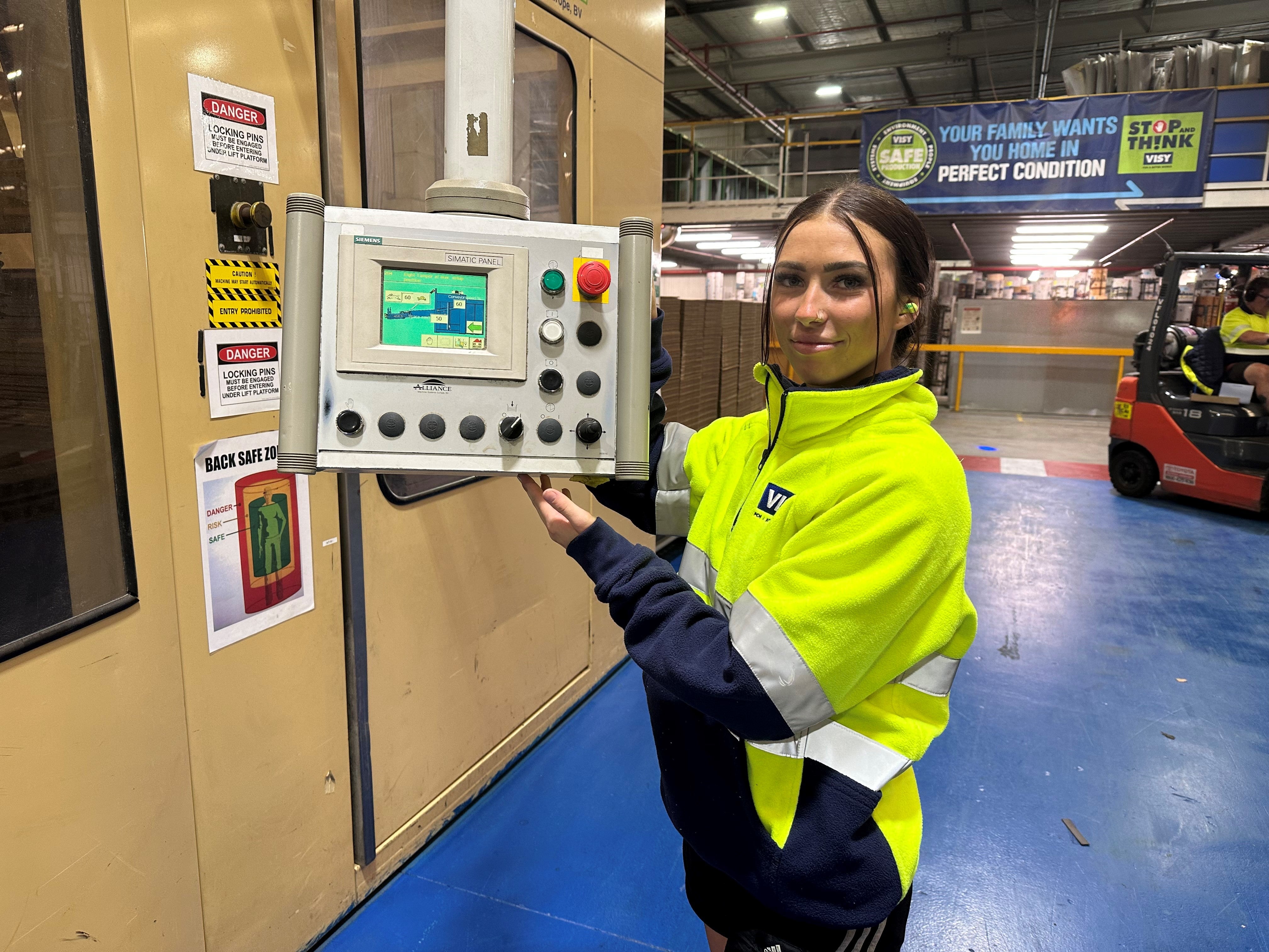Woman with brown hair in yellow high visibility safety jumper smiles at camera holding a control panel