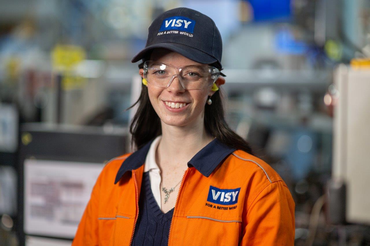 A headshot of a woman in a blue Visy cap, safety glasses and orange high vis top smiles at the camera