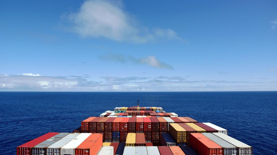 The front of a cargo ship with lots of shipping containers on it, in the open ocean with blue sky