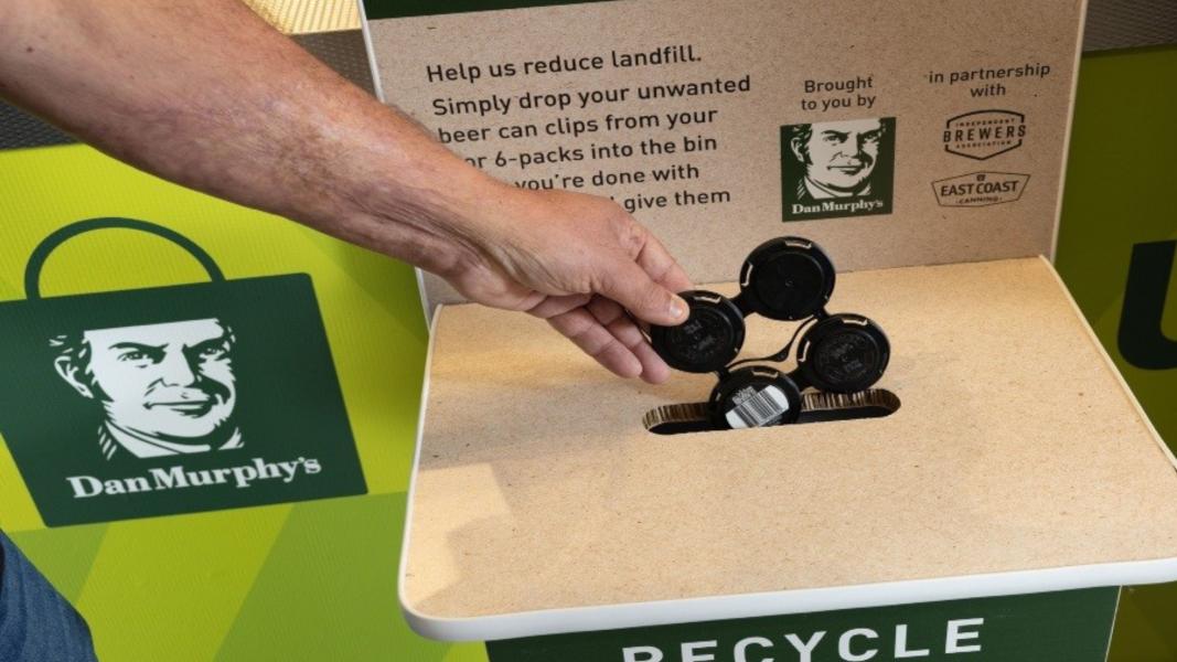 A hand puts a used beer can clip into a recycling bin at Dan Murphy's