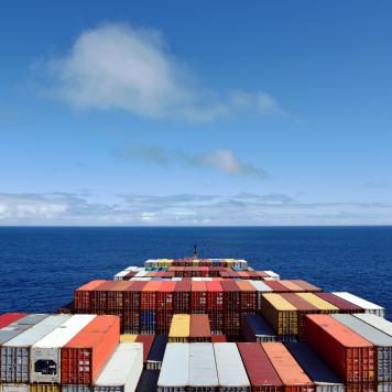 The front of a cargo ship with lots of shipping containers on it, in the open ocean with blue sky