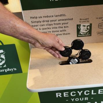 A hand puts a used beer can clip into a recycling bin at Dan Murphy's