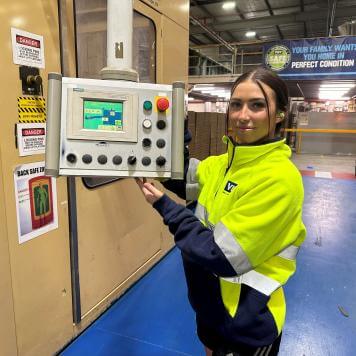 Woman with brown hair in yellow high visibility safety jumper smiles at camera holding a control panel