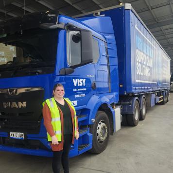 Woman standing in front of blue truck in yellow hi-vis 