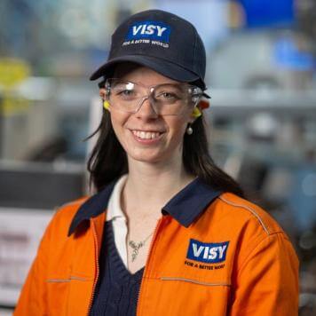 A headshot of a woman in a blue Visy cap, safety glasses and orange high vis top smiles at the camera