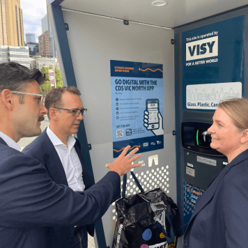 Two men and a woman are talking in front of a blue reverse vending mahcine