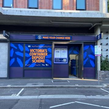 Image of The District Docklands Reverse Vending Machine shop front, in Victoria's Container Deposit Scheme branding of Blue and Orange